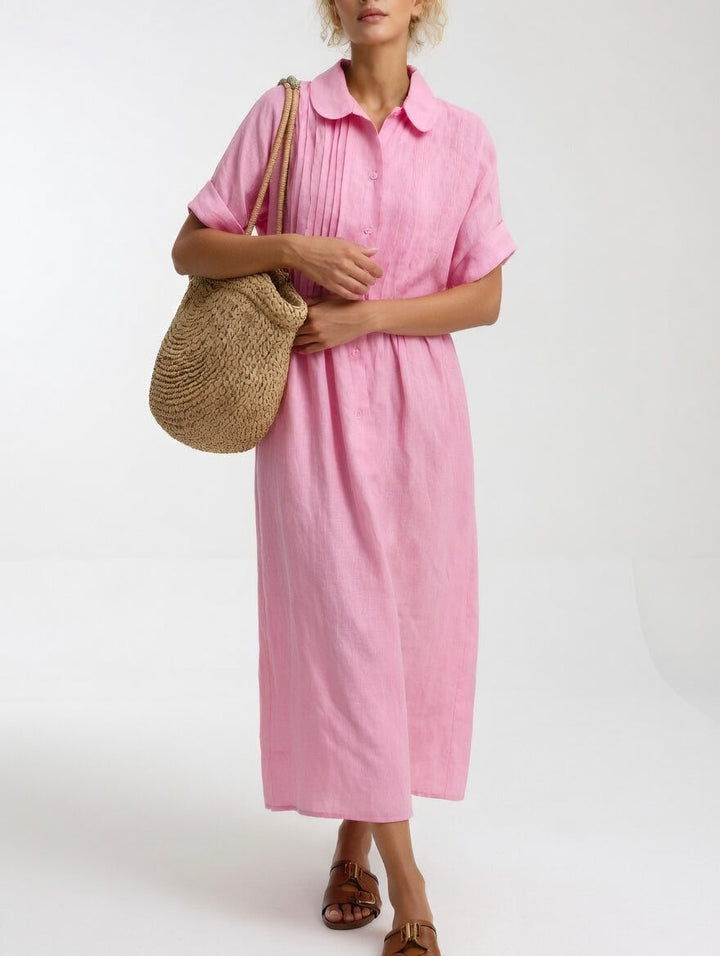 Das Hemdkleid in Rosa von vorn, getragen mit Strohtasche über der Schulter und verschränkten Händen vor dem Körper. 4