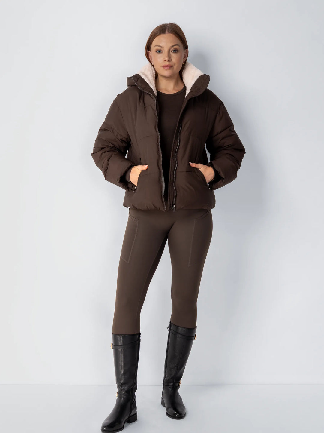 Ganzkörperansicht der braunen Steppjacke, offen getragen, mit braunen Leggings und schwarzen Reitstiefeln 15