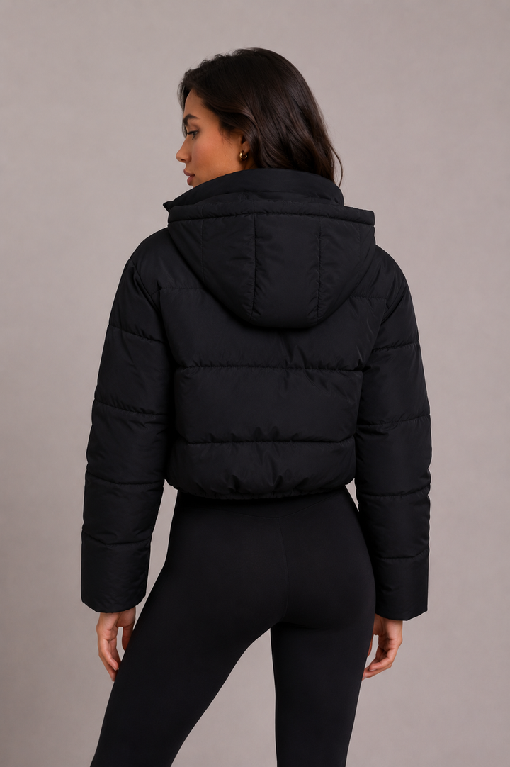 Rückansicht der kurzen schwarzen Steppjacke mit Kapuze und waagerechten Steppnähten, Model blickt über die Schulter. 4