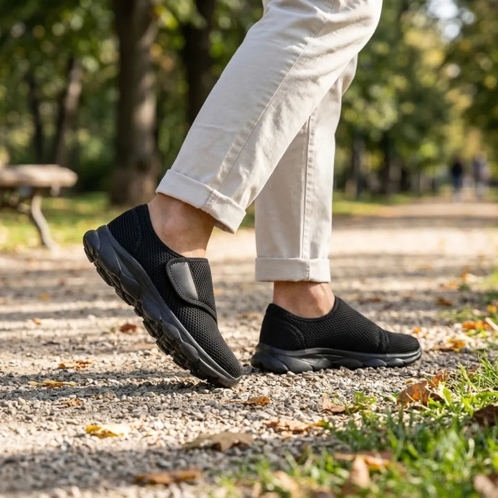 Schwarze Klettschuhe aus Netzstoff mit schwarzer Sohle, getragen beim Gehen auf einem Kiesweg im Park, dazu helle Hose. 11