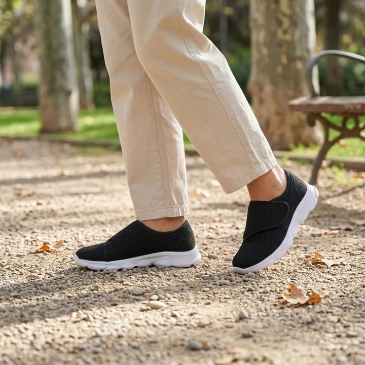 Schwarze Netzschuhe mit Klettverschluss und weißer Sohle, getragen beim Spaziergang auf einem Kiesweg im Park, dazu beige Hose. 20