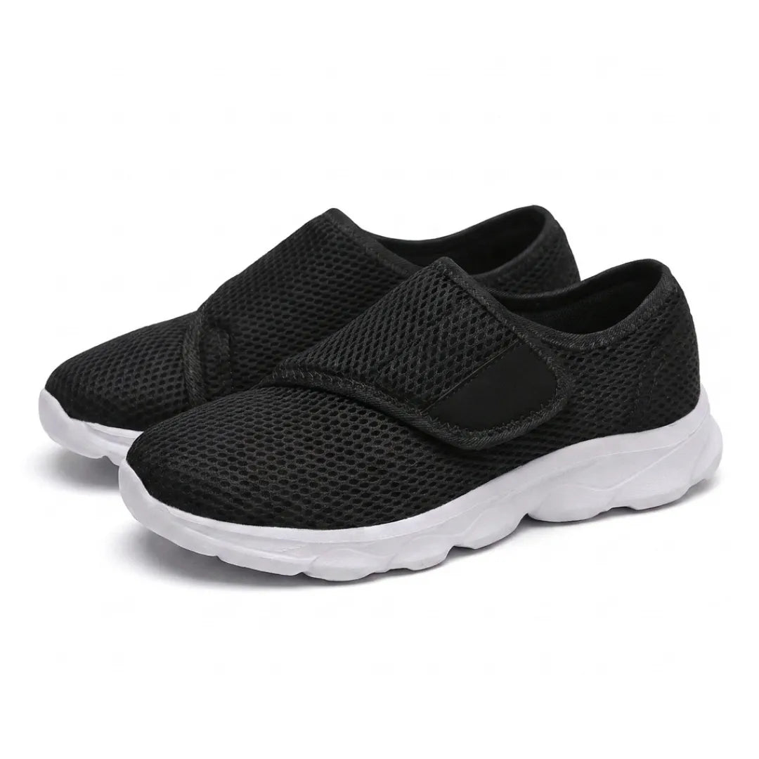 Paar schwarze Mesh-Schuhe mit weißer Sohle und breitem Klettverschluss, schräg von vorn auf weißem Hintergrund fotografiert. 25