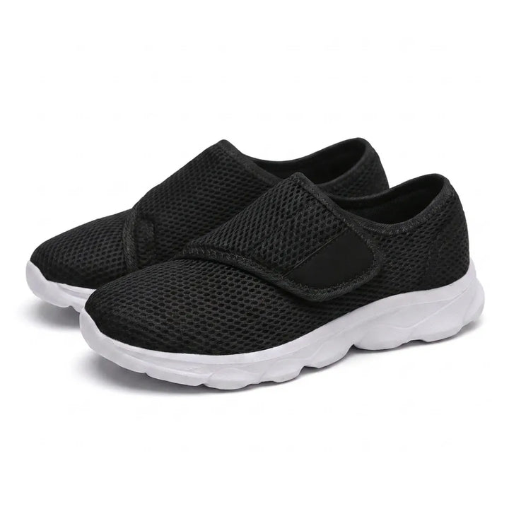 Paar schwarze Mesh-Schuhe mit weißer Sohle und breitem Klettverschluss, schräg von vorn auf weißem Hintergrund fotografiert. 25