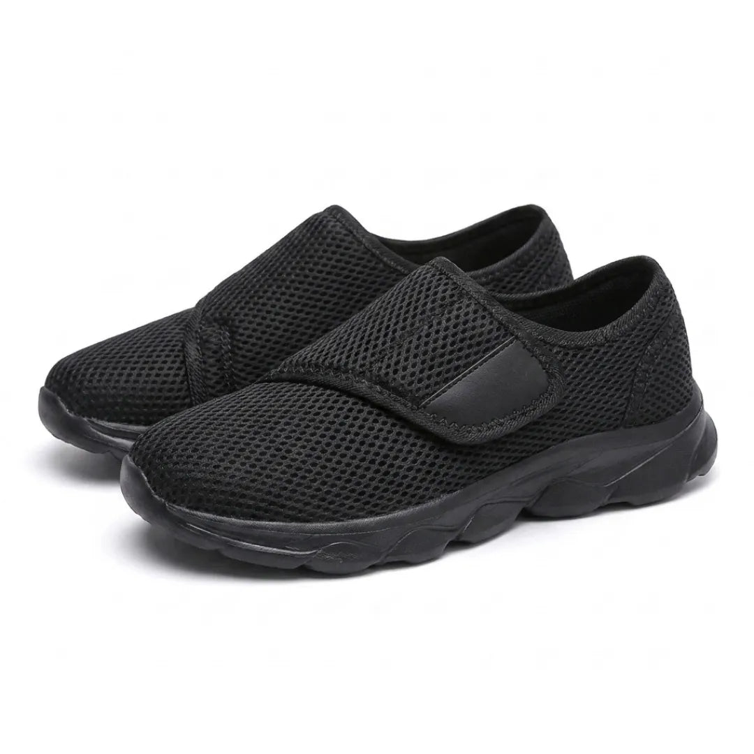 Paar schwarze Netzschuhe mit Klettverschluss und schwarzer Sohle, schräg von vorn nebeneinander fotografiert. 16
