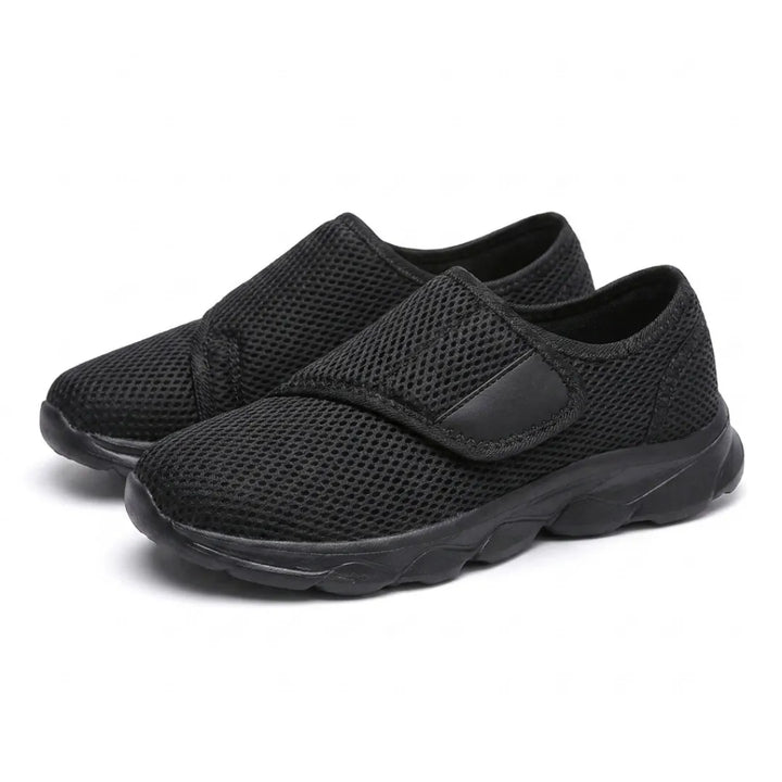 Paar schwarze Netzschuhe mit Klettverschluss und schwarzer Sohle, schräg von vorn nebeneinander fotografiert. 16