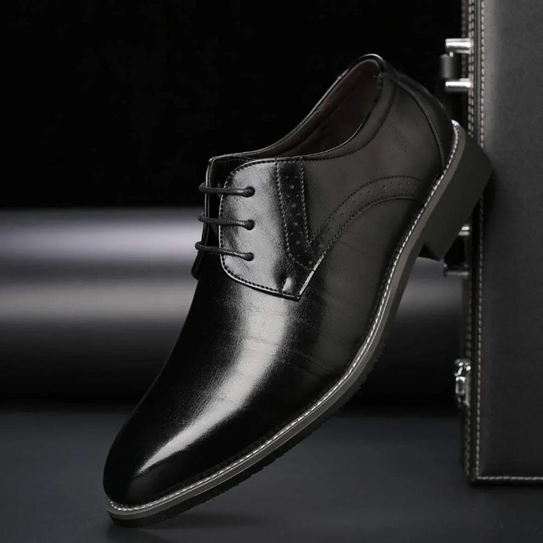 Schwarzer polierter Lederschuh mit Brogue-Lochmuster, an einen dunklen Aktenkoffer gelehnt, Seitenansicht vor schwarzem Hintergrund. 3