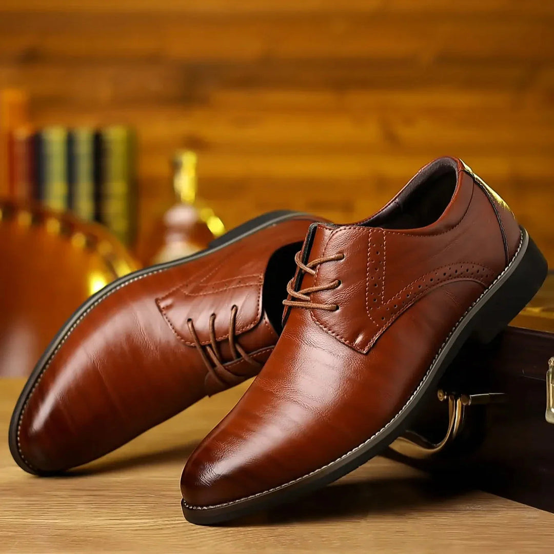 Zwei glänzende cognacbraune Lederschuhe mit Schnürung und Lochmuster, schräg auf einem Holztisch vor warm beleuchtetem Hintergrund arrangiert. 1