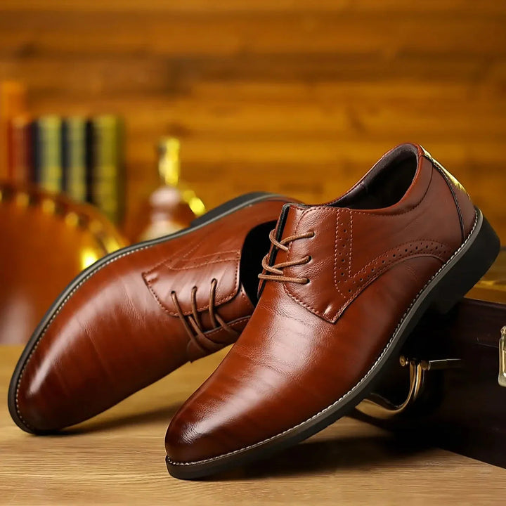 Zwei glänzende cognacbraune Lederschuhe mit Schnürung und Lochmuster, schräg auf einem Holztisch vor warm beleuchtetem Hintergrund arrangiert. 1