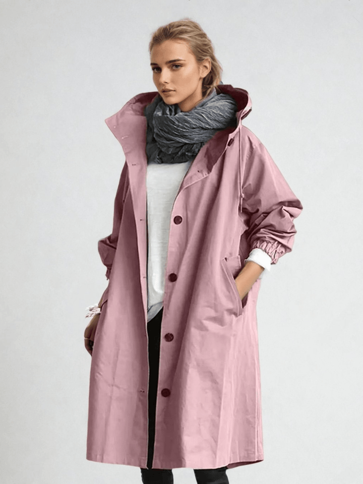 Frontansicht in Rosa: Das Model trägt den knöpfbaren Mantel mit Kapuze über weißem Shirt, grauem Schal und schwarzer Hose. 6