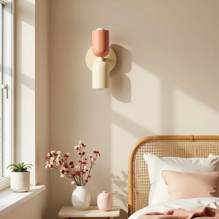 Wandlampe mit lachsfarbenem oberem und cremefarbenem unterem Schirm über einem Nachttisch neben einem Bett mit Rattan-Kopfteil im Sonnenlicht. 2