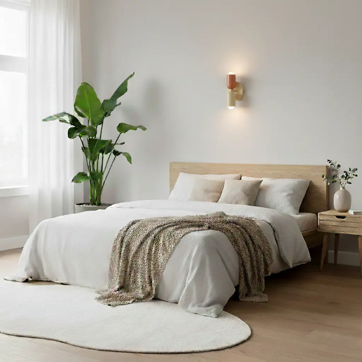 Kleine Wandlampe in Lachs und Creme über einem Bett mit hellem Leinenbezug in einem ruhigen Schlafzimmer mit großer Zimmerpflanze. 8