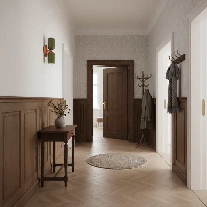 Wandlampe mit zwei grünen Schirmen und lachsfarbenem Arm in einem Flur mit Holzvertäfelung, Konsolentisch, Garderobe und Fischgrätparkett. 7