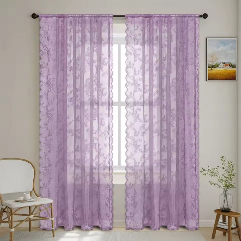 Zwei fliederfarbene Spitzenpaneele mit Blumenmuster und Wellenkante hängen an einer Stange vor einem Fenster im hellen Zimmer. 10