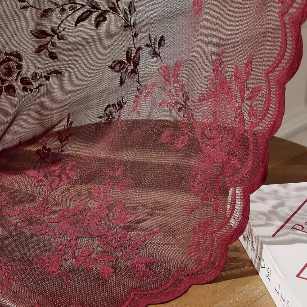 Nahaufnahme der weinroten Spitze mit Rosenranken und gewellter Kante, die auf einem Holztisch neben einem Buch aufliegt. 3