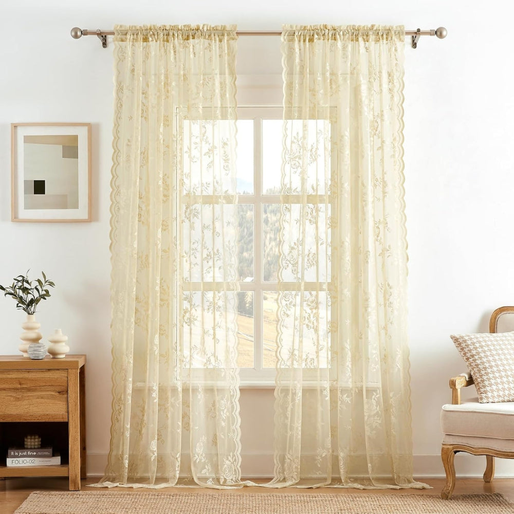 Zwei cremefarbene Spitzenpaneele mit zartem Blumenmuster an einer Stange vor einem großen Fenster, daneben Sessel und Regal. 8