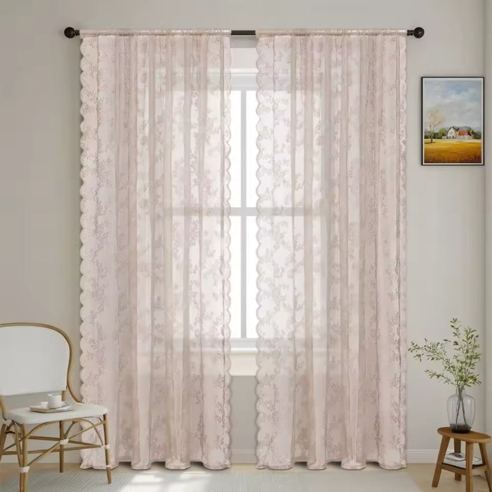 Zwei zartrosa Spitzenpaneele mit feinem Blumenmuster und Wellenkante hängen vor einem Fenster neben Stuhl und Pflanze. 9