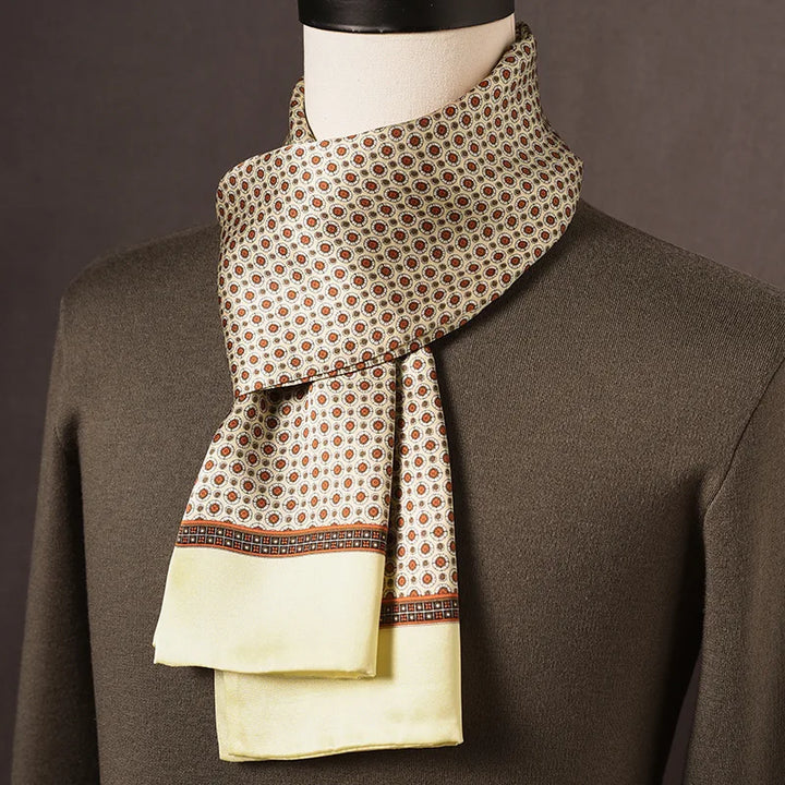 Heller Seidenschal mit orangebraunen Medaillonmotiven und hellgelbem Rand, über olivgrünem Pullover an einer Büste drapiert. 9