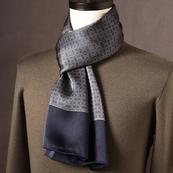 Grau-blauer Seidenschal mit geometrischem Mäandermuster und marineblauem Rand, an einer Büste über olivgrünem Pullover. 10