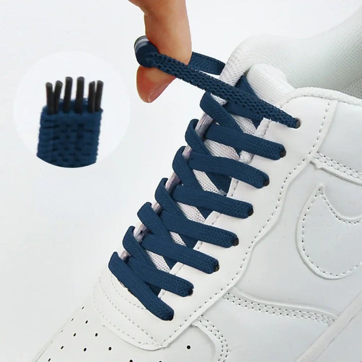Flache dunkelblaue Schnürsenkel an weißem Sneaker, eine Hand hält das Ende, Vergrößerung zeigt die Gewebestruktur 1