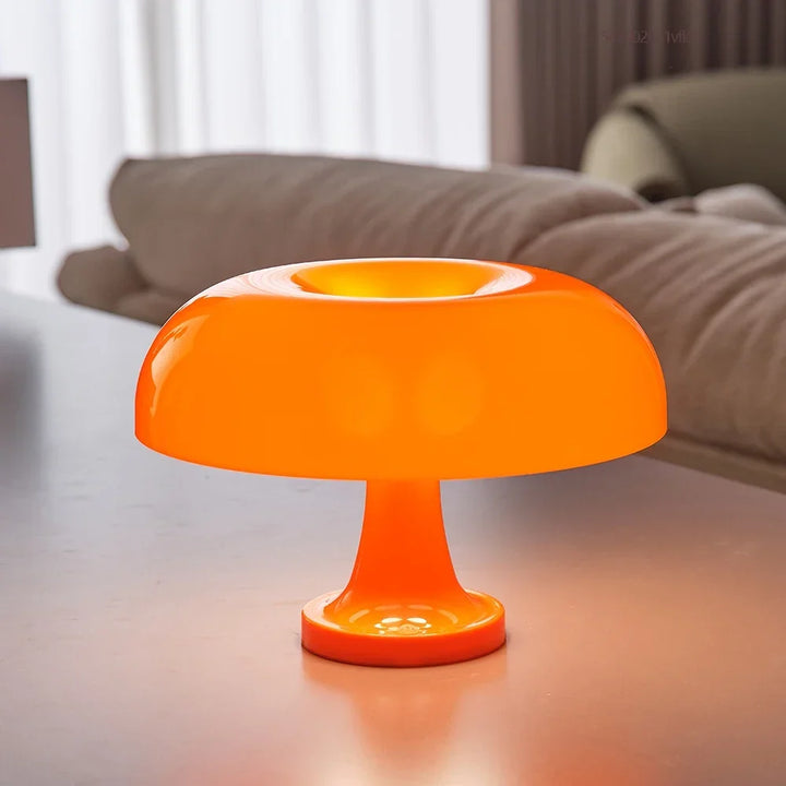 Orange leuchtende Pilzlampe in Nahaufnahme auf einem Tisch, im Hintergrund ein Sofa mit beigen Kissen. 3