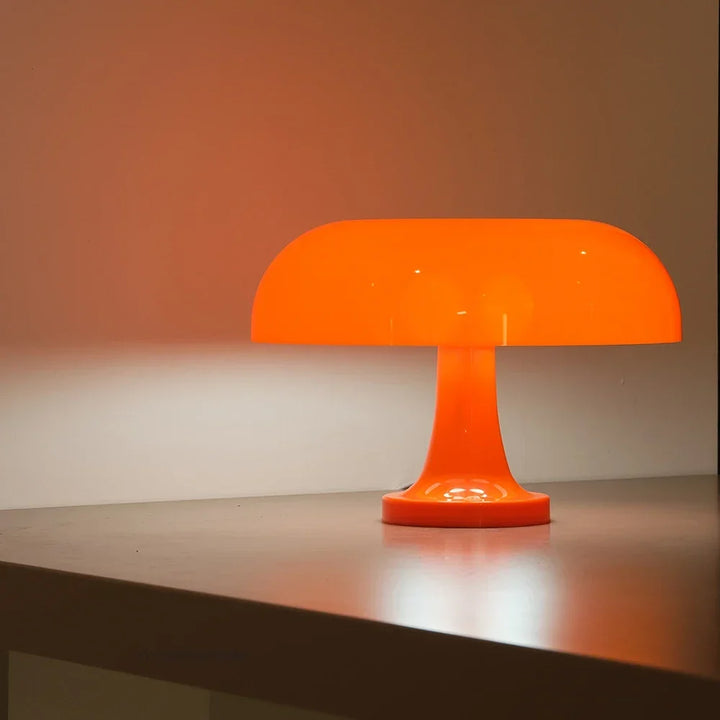 Seitenansicht der orange leuchtenden Pilzlampe auf einer Tischkante vor einer warm angestrahlten Wand. 6