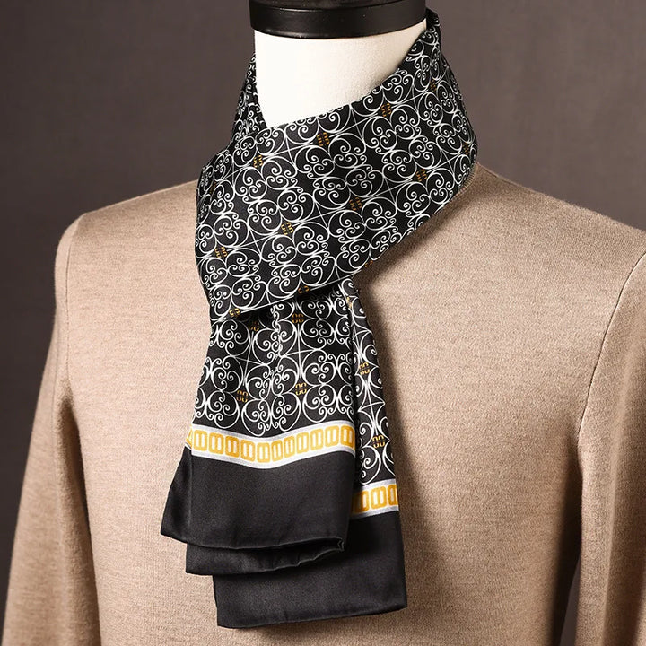Schwarzer Seidenschal mit weißem Ornamentmuster und gelber Bordüre, an einer Büste über beigem Pullover um den Hals gelegt. 25