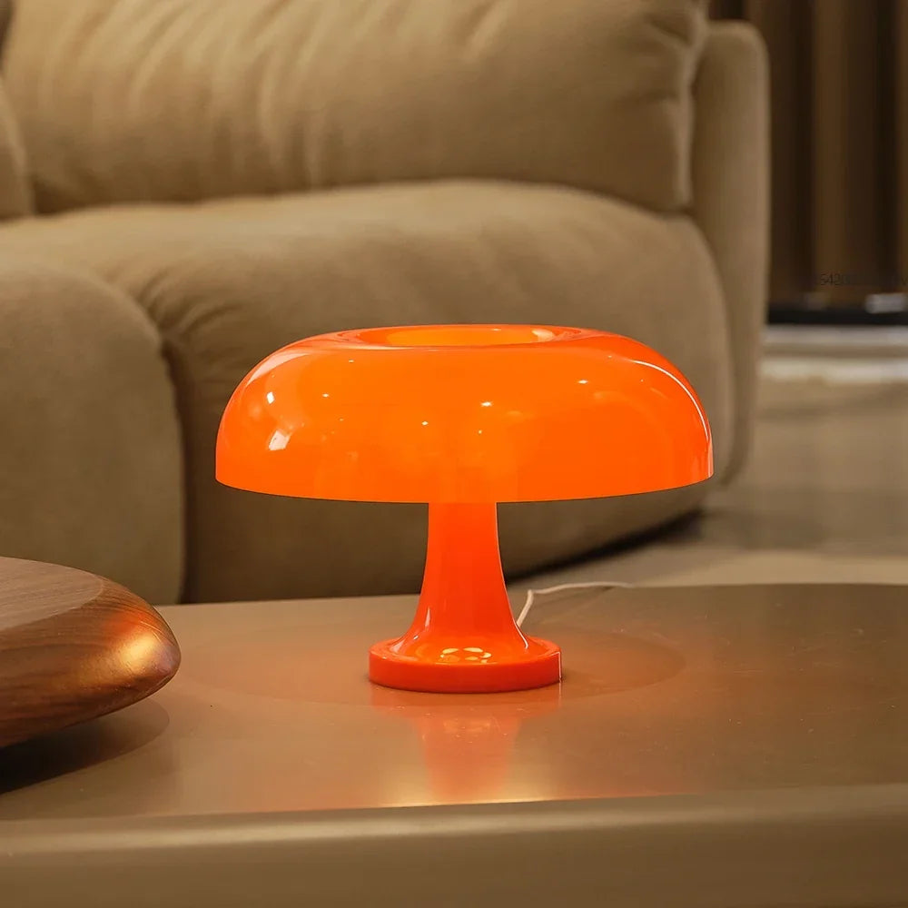 Orange Pilzlampe mit glänzendem Schirm und sichtbarem weißem Kabel auf einem Tisch vor einem beigen Sofa. 5