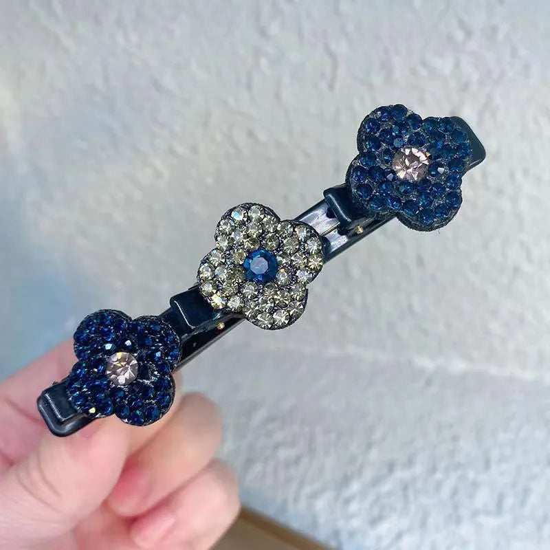 Einzelne Haarspange mit drei Strassblüten in Marineblau und Grau, vor heller Wand in der Hand gehalten. 3