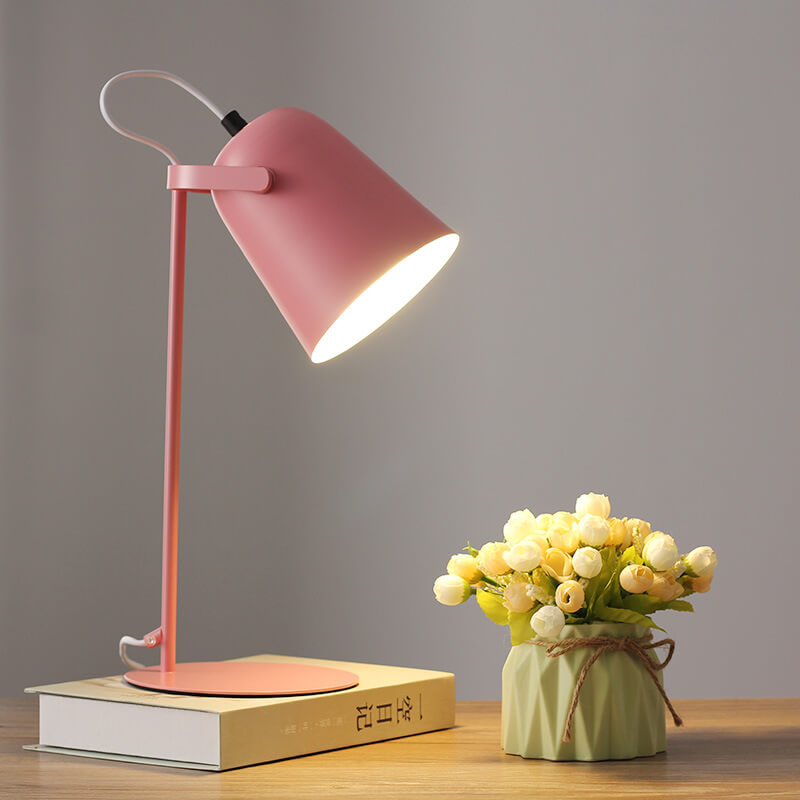 Rosafarbene Tischlampe mit eingeschaltetem Licht auf einem Buch, daneben eine Vase mit hellen Röschen auf einem Holztisch. 8