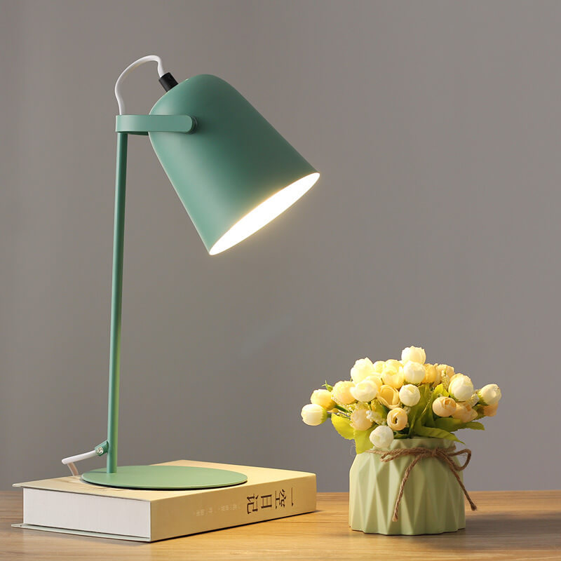 Grüne Tischlampe mit eingeschaltetem Licht auf einem Buch, daneben eine Vase mit cremefarbenen Röschen. 9