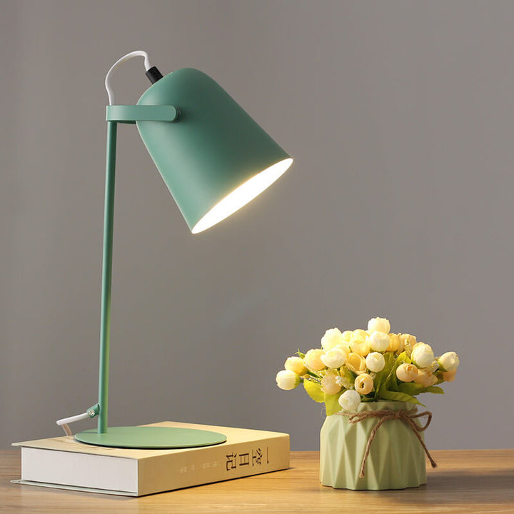Grüne Tischlampe mit eingeschaltetem Licht auf einem Buch, daneben eine Vase mit cremefarbenen Röschen. 9