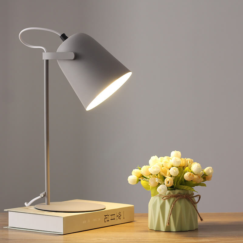 Graue Tischlampe mit eingeschaltetem Licht auf einem Buch, daneben eine grüne Vase mit hellen Röschen. 10