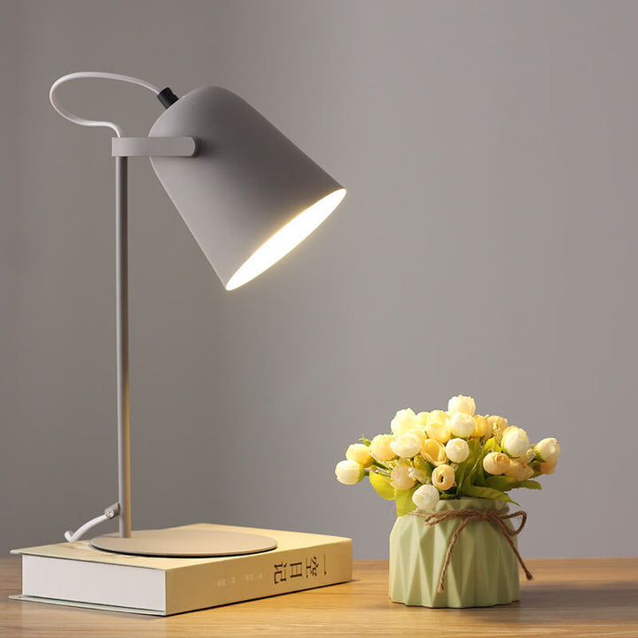 Graue Tischlampe mit eingeschaltetem Licht auf einem Buch, daneben eine grüne Vase mit hellen Röschen. 10
