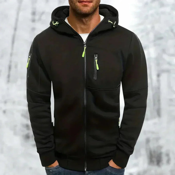 Schwarzer Kapuzenpullover mit neongrünen Reißverschlussziehern an Brusttasche und Ärmeltasche, von einem Mann vor Winterhintergrund getragen. 7
