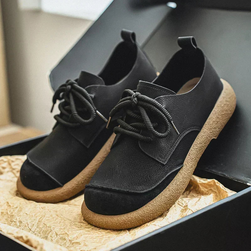 Schwarze Schnürschuhe mit heller Gummisohle und dunkler Kappe in einer geöffneten Schuhschachtel auf Packpapier. 12
