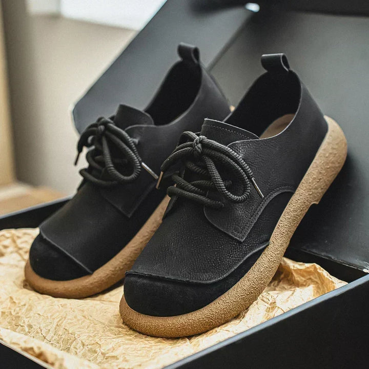Schwarze Schnürschuhe mit heller Gummisohle und dunkler Kappe in einer geöffneten Schuhschachtel auf Packpapier. 12