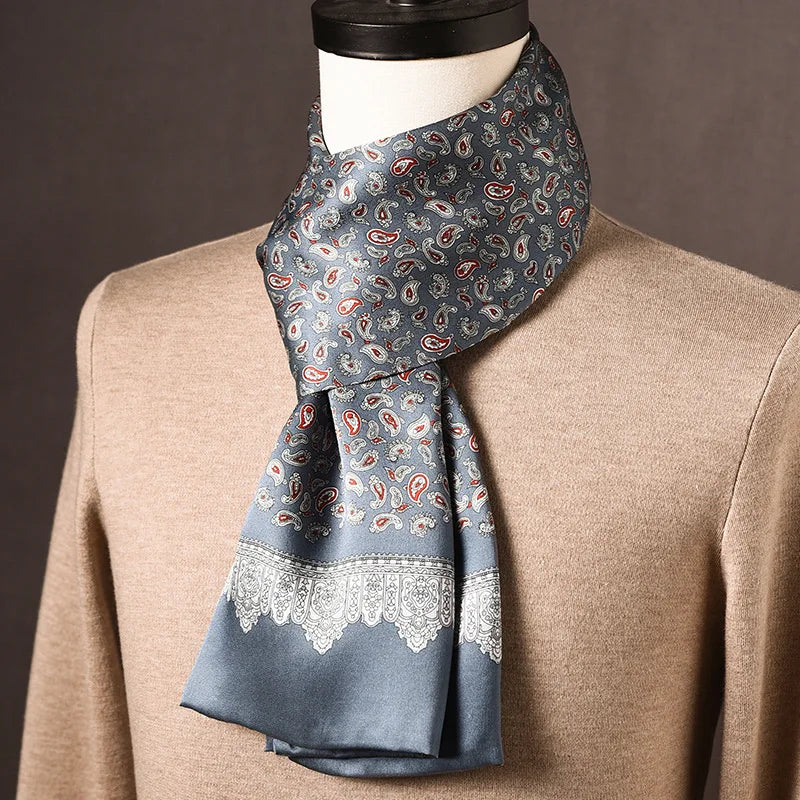 Grauer Seidenschal mit rot-weißem Paisleymuster und heller Spitzenbordüre, über beigem Pullover an einer Büste drapiert. 18