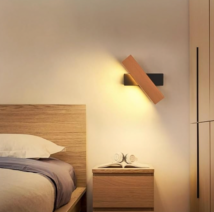 Schräg gedrehte Holzleuchte mit schwarzer Halterung über einem Nachttisch neben einem Holzbett, Kopfhörer auf einem Buch. 6
