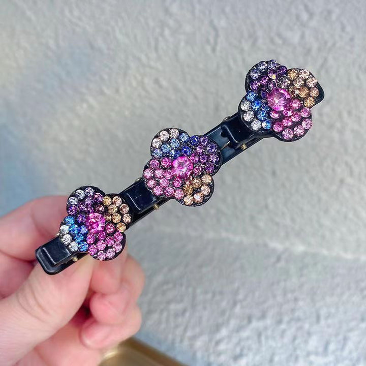 Einzelne Haarspange mit drei bunten Strassblüten in Rosa, Blau, Lila und Gold, vor heller Wand in der Hand gehalten. 5