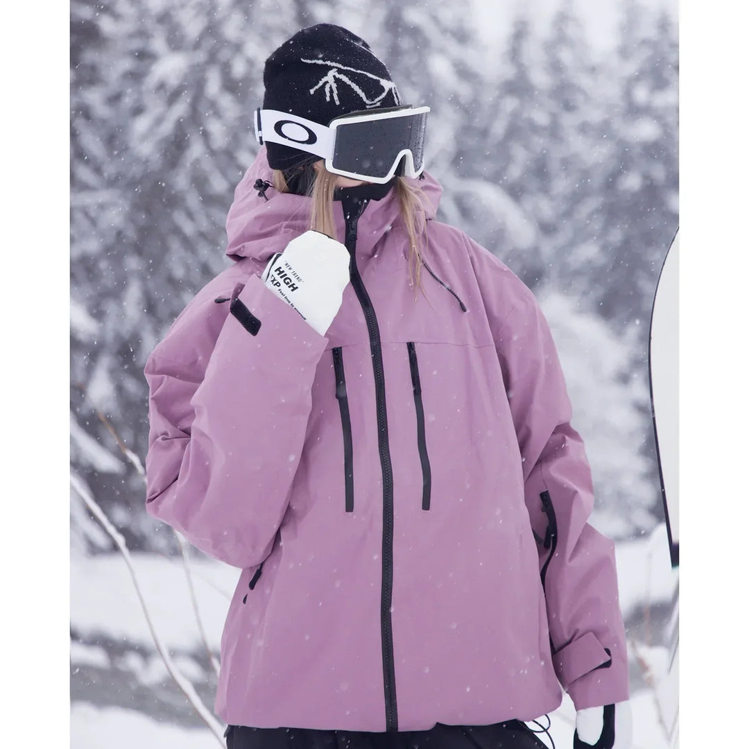 Nahaufnahme der rosafarbenen Skijacke an einer Person mit Skibrille, weißen Handschuhen und Brusttaschen mit schwarzen Reißverschlüssen im Schneefall. 4