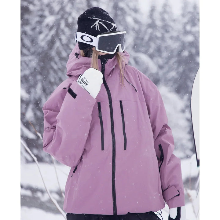 Nahaufnahme der rosafarbenen Skijacke an einer Person mit Skibrille, weißen Handschuhen und Brusttaschen mit schwarzen Reißverschlüssen im Schneefall. 4