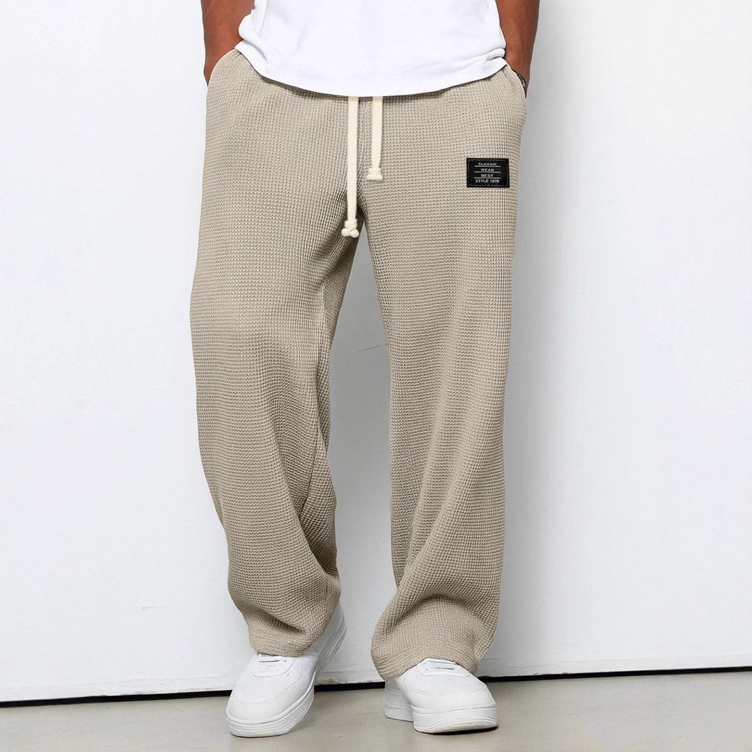 Die Hose in Beige, leicht schräg fotografiert, mit weitem Bein, Kordelzug und weißen Sneakern. 6
