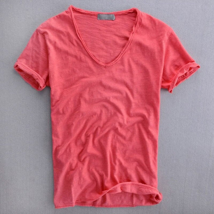Korallrotes Kurzarm-Shirt mit V-Ausschnitt, flach auf grauem Untergrund fotografiert, mit sichtbarer Garnstruktur und umgeschlagenen Ärmelsäumen. 3