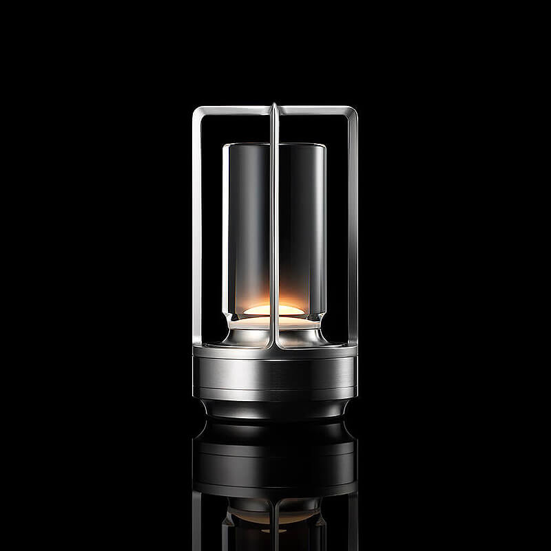 Leuchtende Tischlampe in Silber mit Metallrahmen und Glaszylinder, freigestellt vor schwarzem Hintergrund. 10