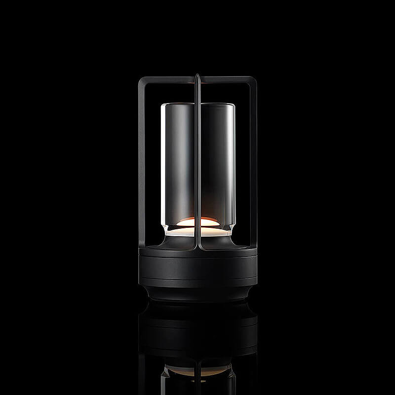 Leuchtende Tischlampe in Schwarz mit Metallrahmen und Glaszylinder, freigestellt vor schwarzem Hintergrund. 11
