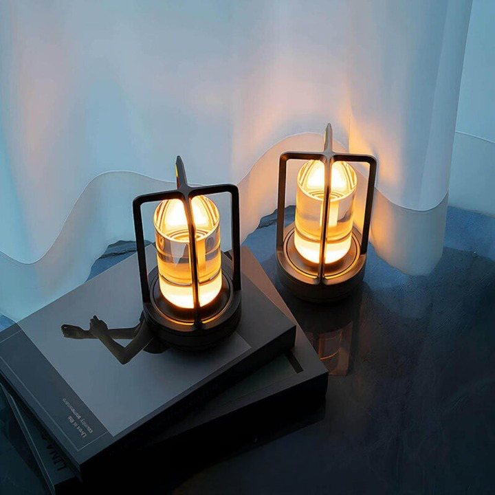 Zwei leuchtende dunkle Lampen mit Metallrahmen stehen auf gestapelten Büchern vor einem hellen Vorhang. 3