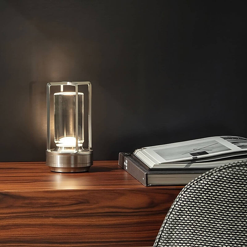 Silberfarbene Lampe leuchtet auf einem Holzsideboard neben aufgeschlagenen Büchern vor dunkler Wand. 5