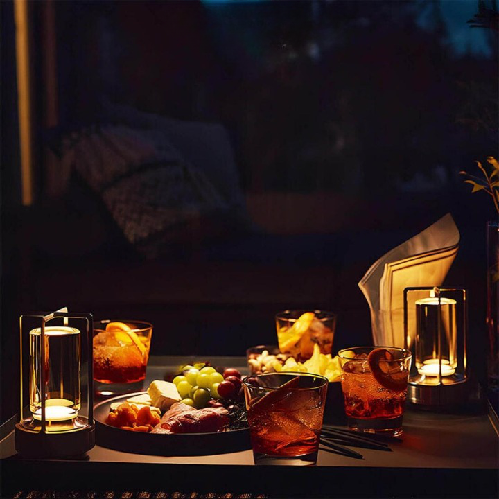 Zwei leuchtende Lampen auf einem abendlichen Tisch mit Aperitif-Gläsern, Trauben, Käse und Aufschnitt. 6