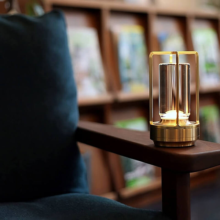 Goldene Lampe leuchtet auf der Holzarmlehne eines Sessels mit blauem Kissen, im Hintergrund ein Bücherregal. 8