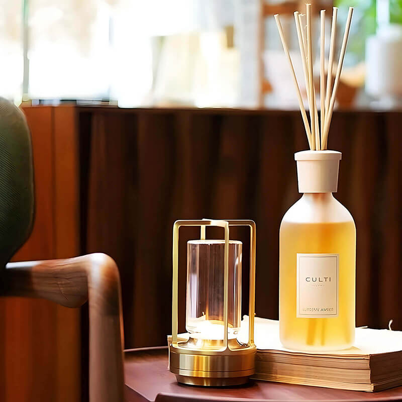 Goldene Lampe leuchtet auf einem Beistelltisch neben einem Raumduft-Diffusor mit Rattanstäbchen und einem Buch. 9